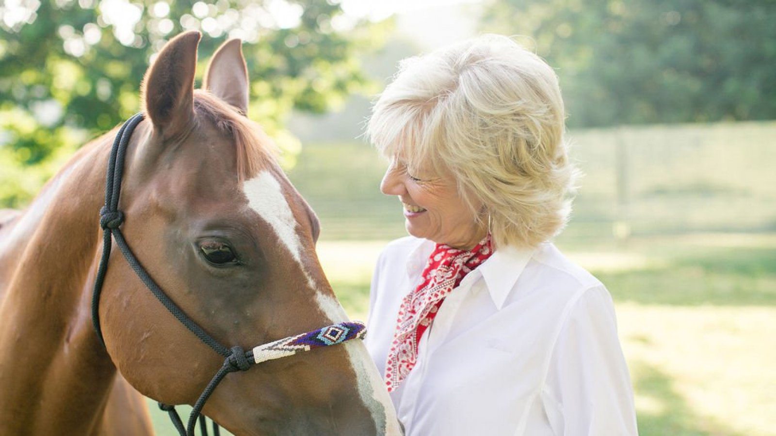 person smiling and standing beside horse