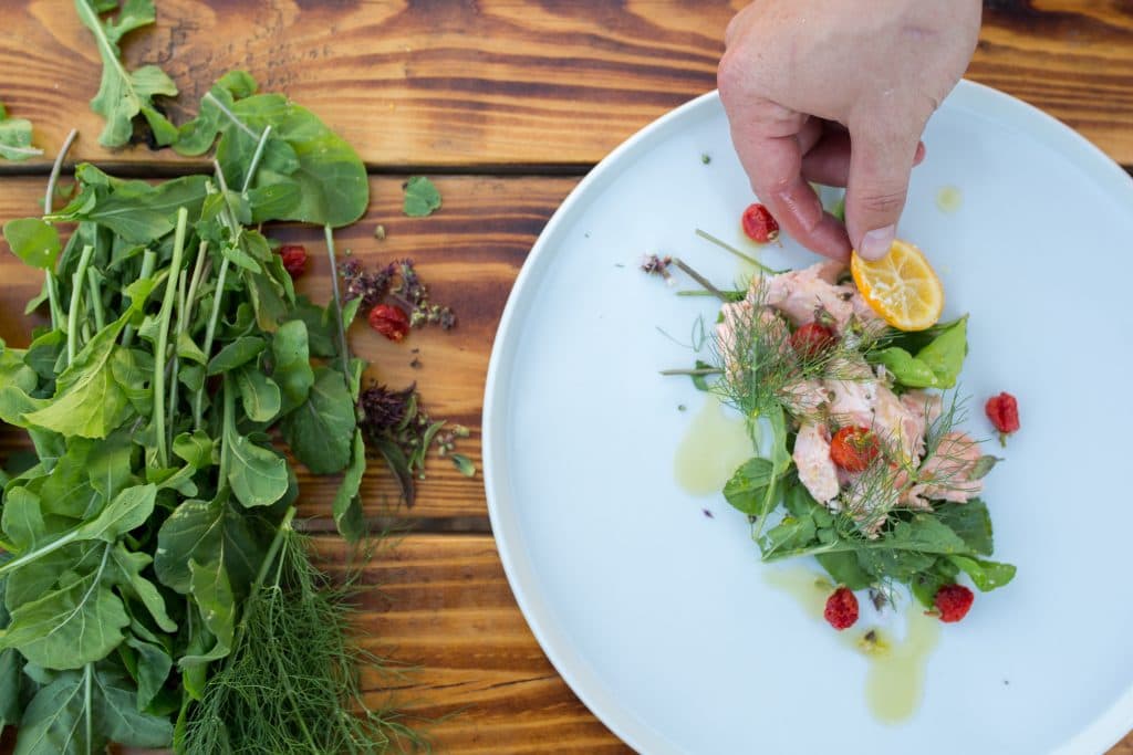 person's hand garnishing the fish and vegetables on a plate