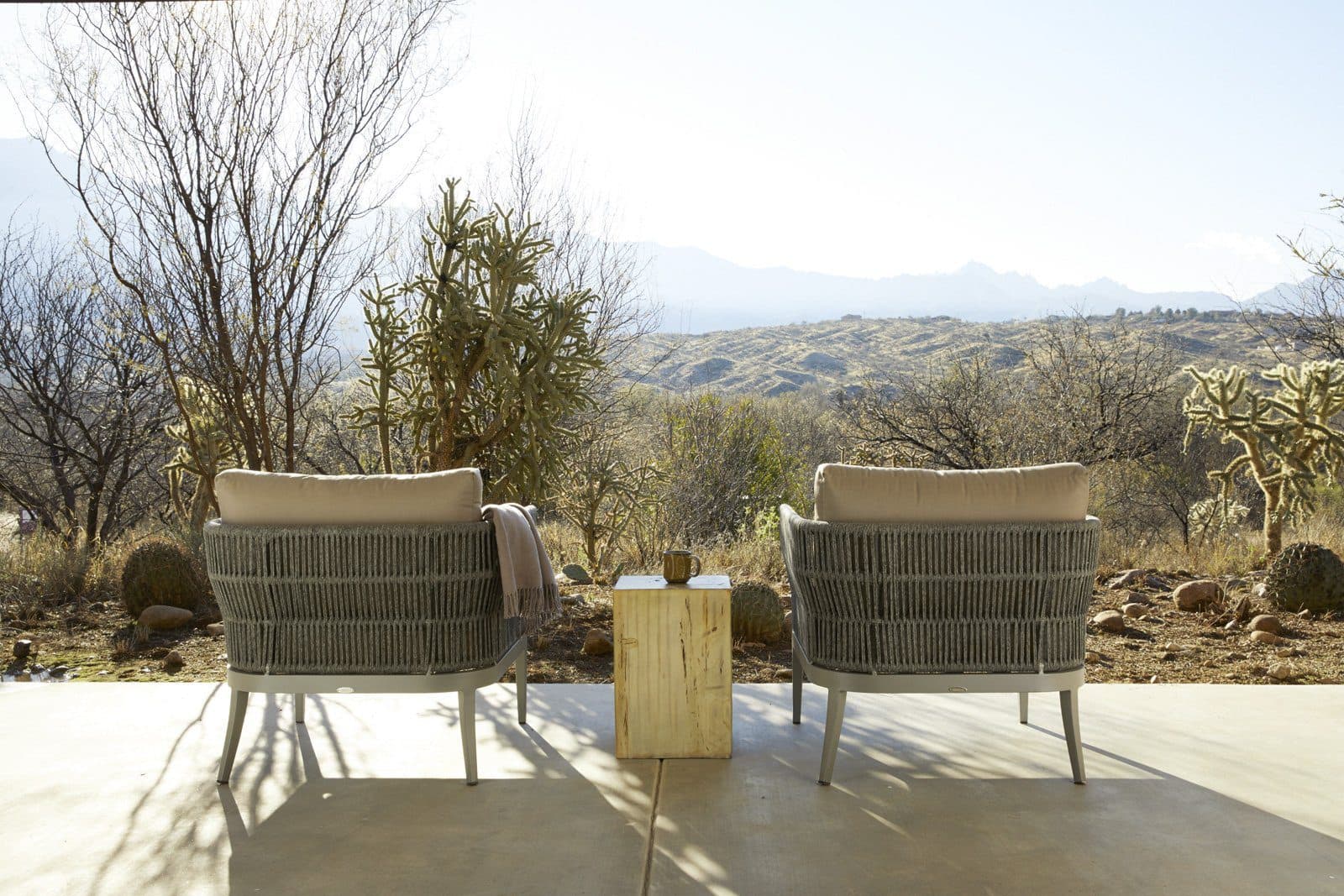 Two lounge chairs in front of desert landscape on patio and small table on