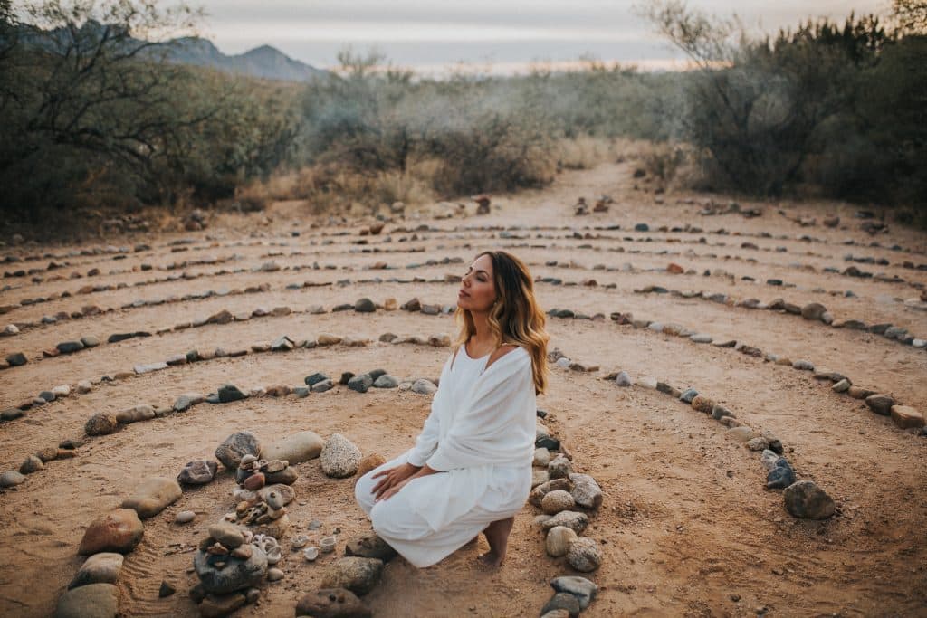 Woman with closed eyes sitting in stone labyrinth in desert