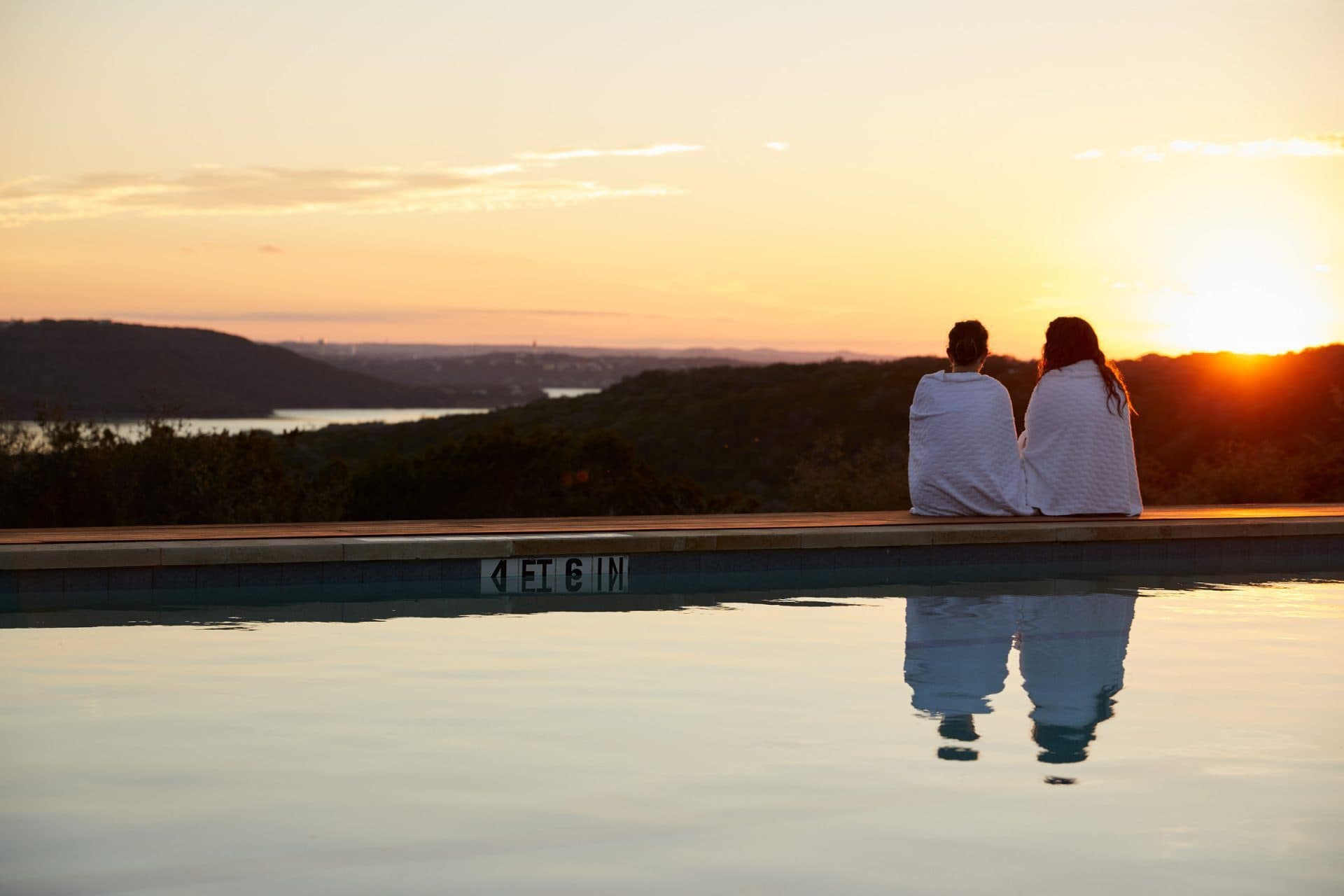 two people in robes sitting by the pool watching the sunset
