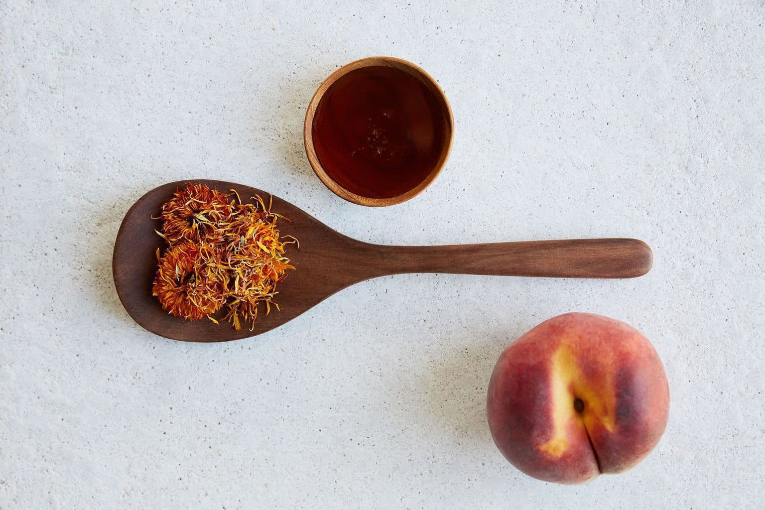 A little bowl of honey, calendula on wooden spoon and peach