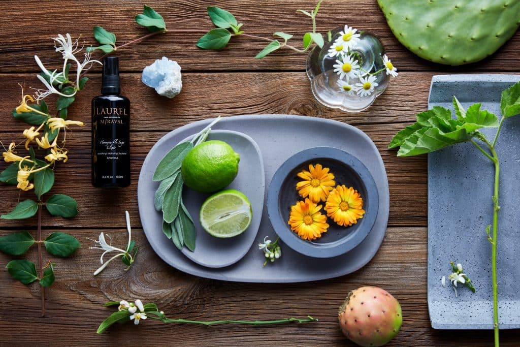 Flower decorations and Honeysuckle sage elixir spray bottle on wood and yellow flowers and lime on plate 