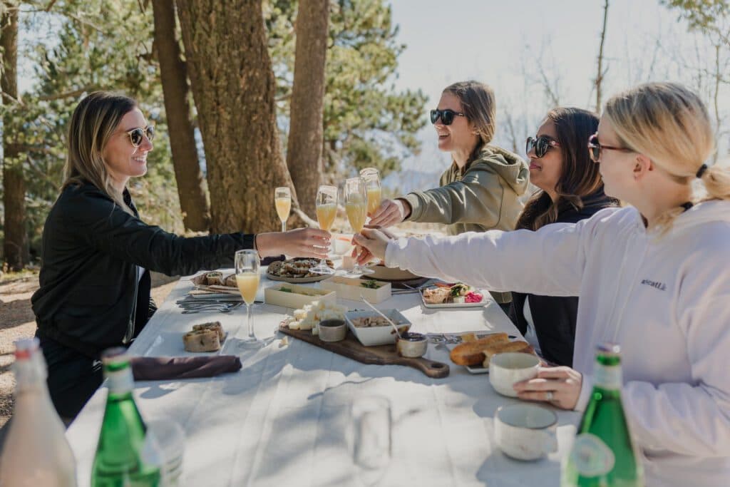 Group of women having food outside on table toasting with mimosas