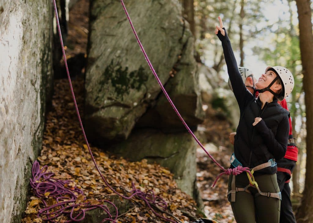 Rock climber in climbing gear pointing to something on rock