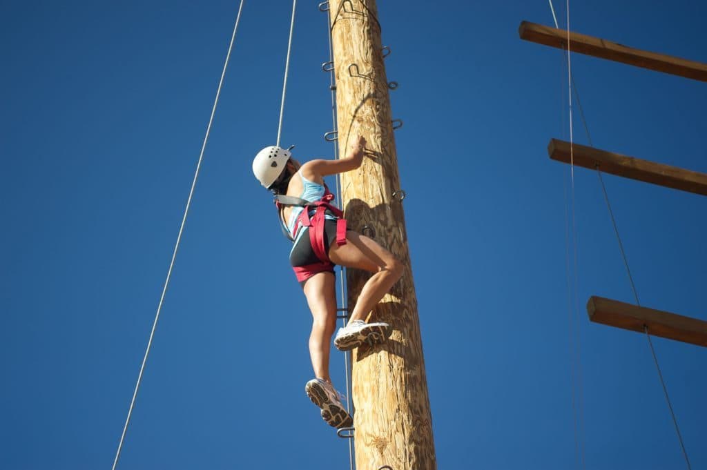 Person with climbing gear on quantum leap course climbing up a pole